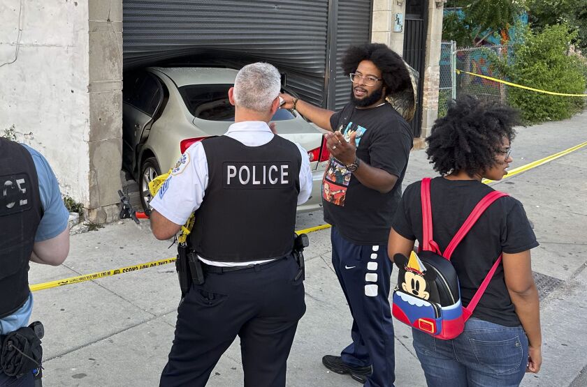 Joe Black and his wife, Tonya, talk to Chicago police officials in front of a car that has crashed through the front window of their restaurant.