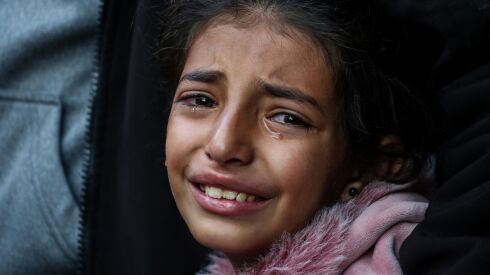 A young Palestinian girl cries as an adult holds her shoulder.