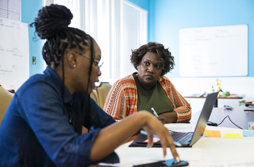 Lashone Kelly talks with executive assistant LaCreshia Birts in person, while also talking on a Zoom call on a laptop. 